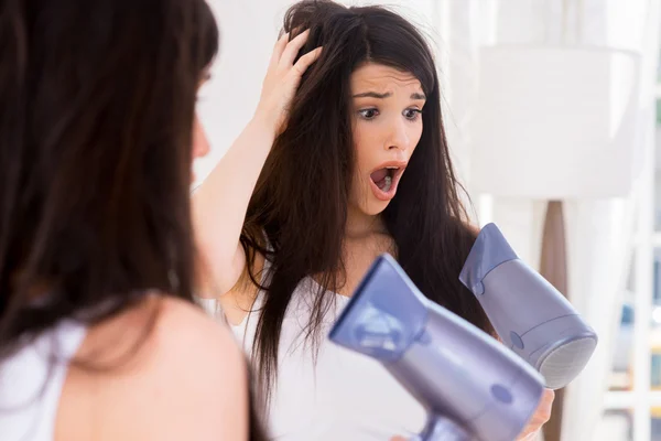 Donna scioccata guardando i capelli asciugacapelli — Foto Stock