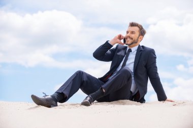 kum üzerine oturan cep telefonu konuşurken işadamı