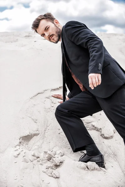 Людина в офіційному вбранні, що піднімається пустельною дюною — стокове фото