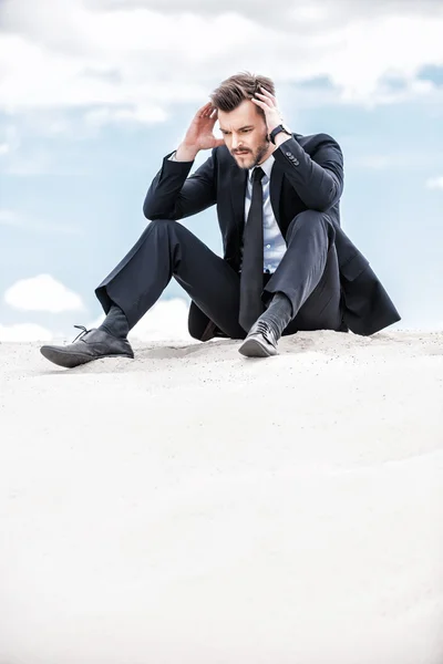 Depressed and confused businessman sitting on sand dune — Stock Photo, Image