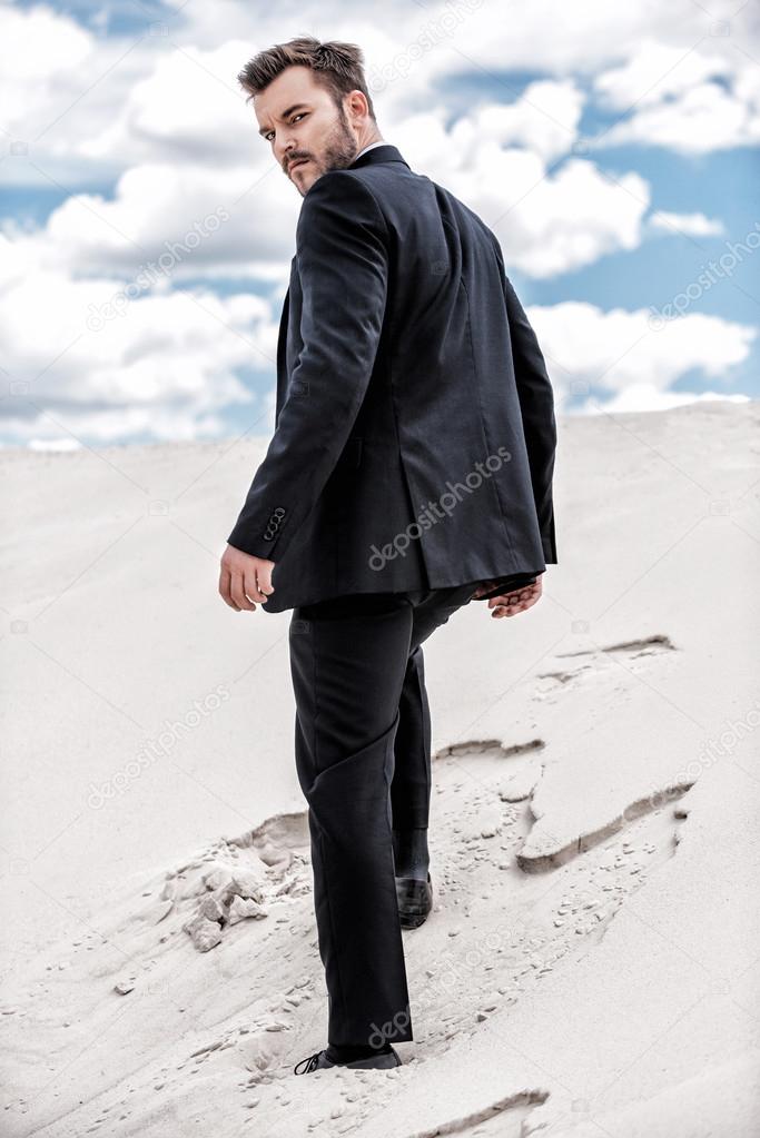 Man in formal wear rising up by desert dune