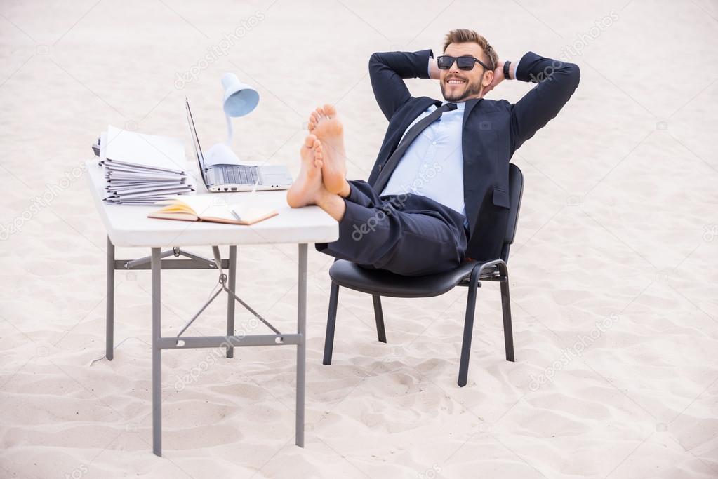 Man in formal wear and sunglasses holding his feet on table