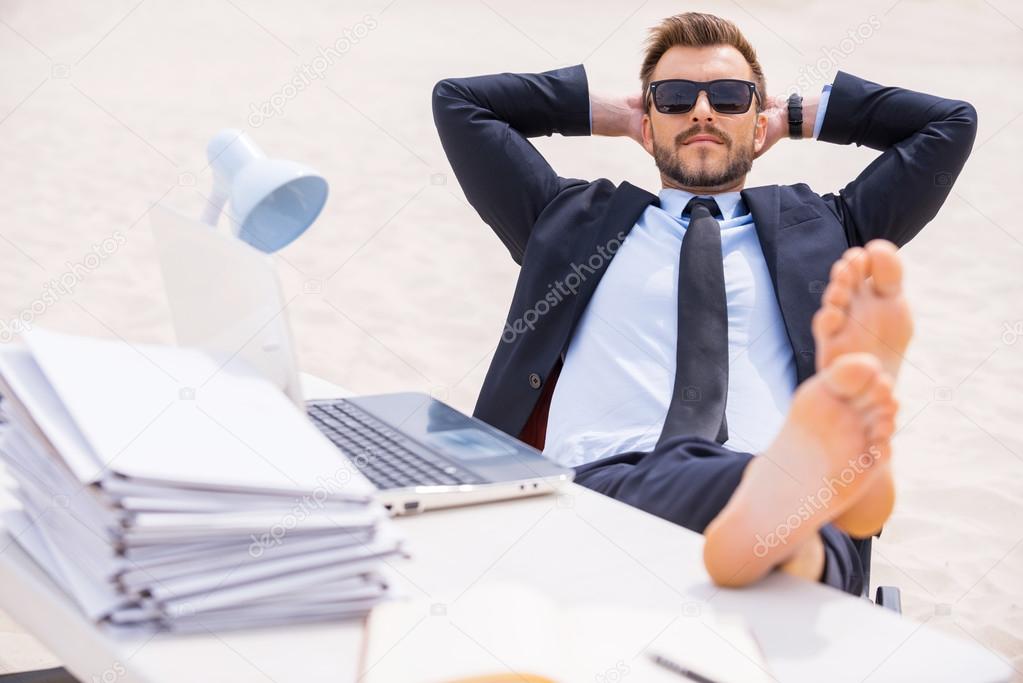 Man in formal wear and sunglasses holding his feet on table