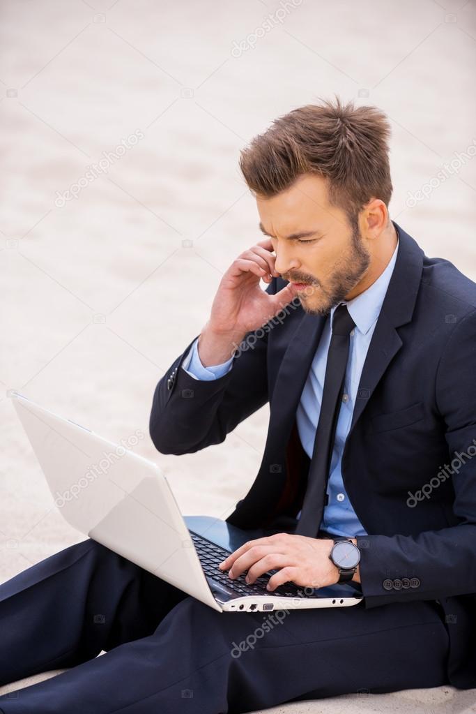 Man in formal wear working on laptop sitting on sand