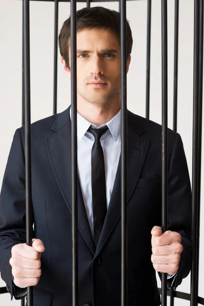 Man in formalwear standing behind a prison cell