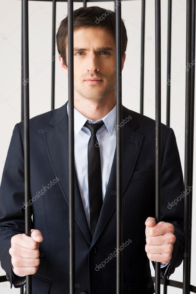 Man in formalwear standing behind a prison cell