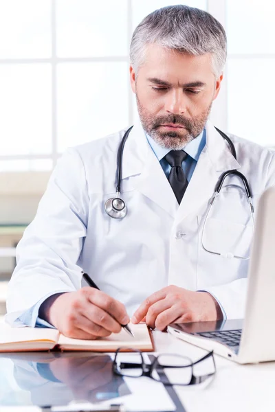 Mature grey hair doctor writing in note pad — Stock Photo, Image