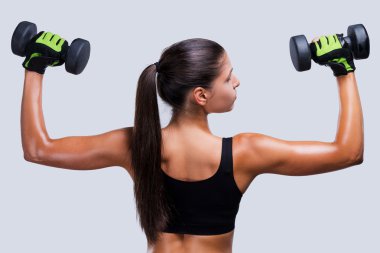 Dambıllarla egzersiz yapan sportif bir kadın.