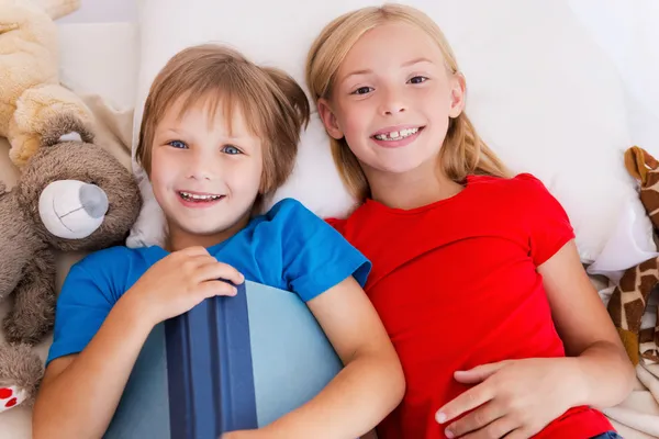 Niños sosteniendo libro mientras están acostados en la cama —  Fotos de Stock