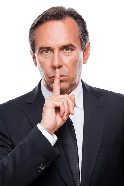 Confident mature businessman holding finger on lips — Stock Photo, Image