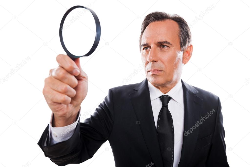 Concentrated businessman looking through magnifying glass