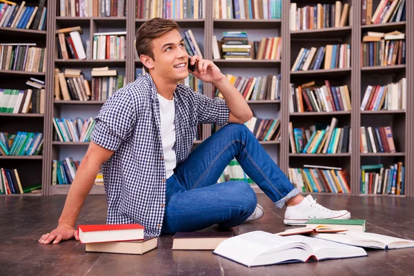 Glad ung man sitter mot bokhyllan — Stockfoto
