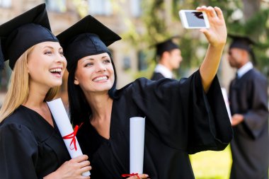 happy women in graduation gowns making selfie