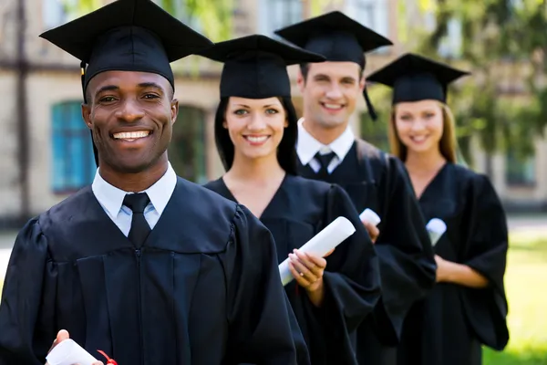 Graduados universitarios de pie en fila y sonriendo — Foto de Stock