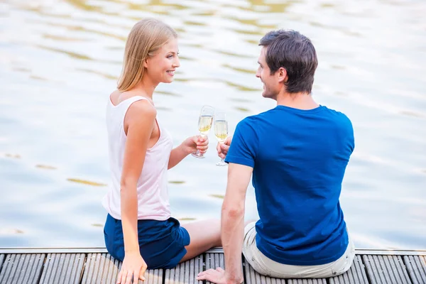 Casal amoroso sentado no cais e bebendo Champaign — Fotografia de Stock