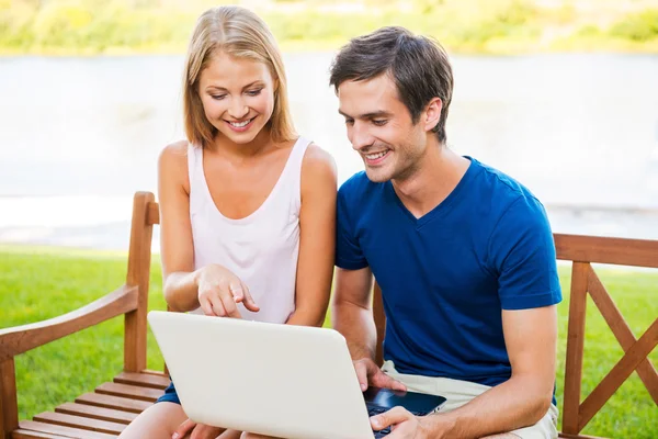 Couple sitting on the bench and looking at laptop — Stock Photo, Image