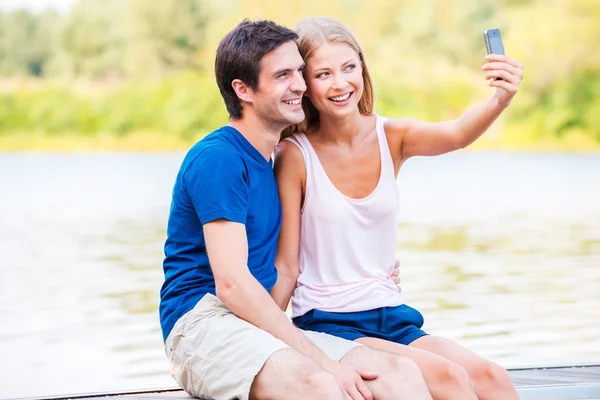 Pareja sentada en el muelle y haciendo selfie —  Fotos de Stock