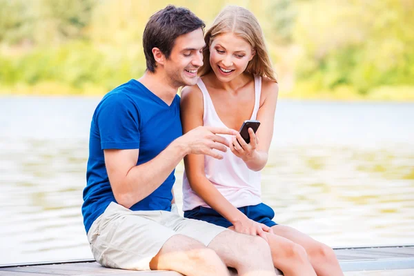 Pareja sentada en el muelle mirando el teléfono móvil —  Fotos de Stock