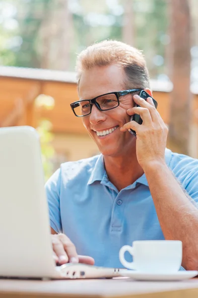 Man working at laptop and talking on mobile phone — Stock Photo, Image