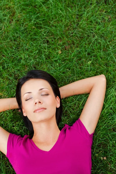 Mladá žena leží na zelené trávě — Stock fotografie