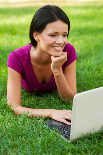 Mulher trabalhando no laptop deitado na grama — Fotografia de Stock