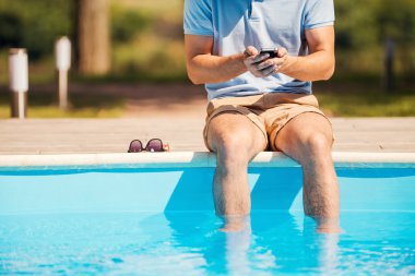 adam havuz üzerinde oturan ve cep telefonu yazarak