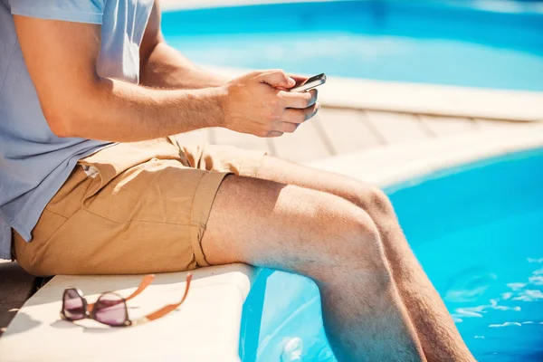 Hombre sentado en la piscina y escribiendo en el teléfono móvil — Foto de Stock