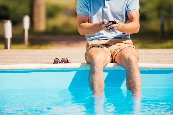 Adam havuz üzerinde oturan ve cep telefonu yazarak — Stok fotoğraf