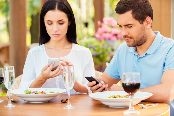 Young couple typing on smart phones in restaurant — Stock Photo, Image