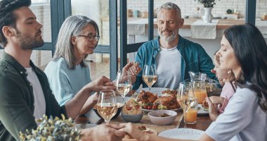 Birlikte yemek yemeden önce el ele tutuşup dua eden mutlu bir aile.
