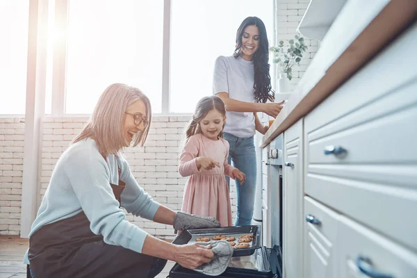 Mooie senior vrouw nemen van koekjes uit de oven en glimlachen terwijl het doorbrengen van tijd met familie — Stockfoto