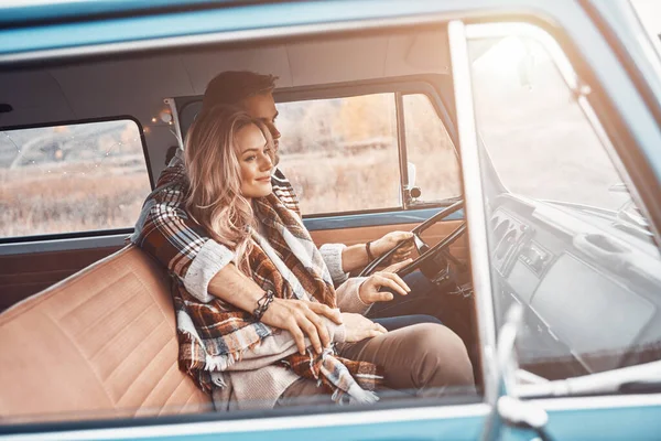 Hermosa pareja amorosa joven disfrutando de viaje por carretera juntos mientras están sentados en los asientos delanteros de la mini furgoneta retro —  Fotos de Stock