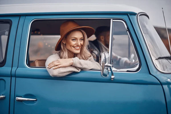 Όμορφη νεαρή γυναίκα κοιτάζει μέσα από ένα παράθυρο και χαμογελά ενώ ο φίλος της οδηγεί ένα αυτοκίνητο — Φωτογραφία Αρχείου
