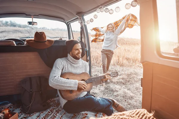 Snygg ung man som spelar gitarr för sin flickvän medan han tillbringar tid i husbil — Stockfoto