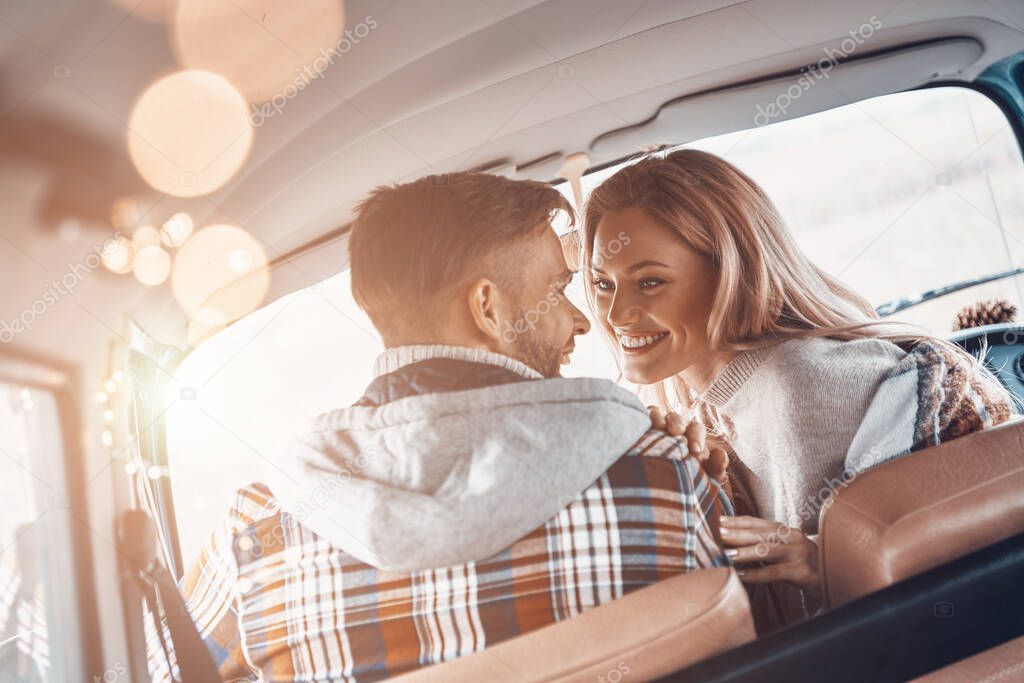 Rear view of beautiful young couple enjoying road trip together while sitting on front seats of minivan