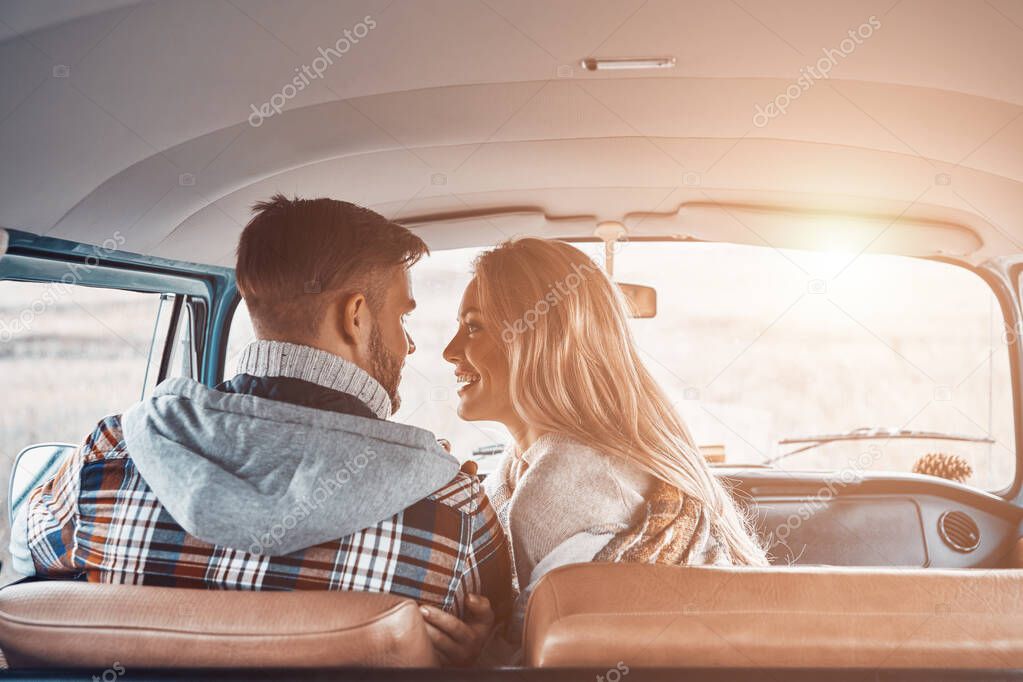 Rear view of beautiful young couple enjoying road trip together while sitting on front seats of minivan