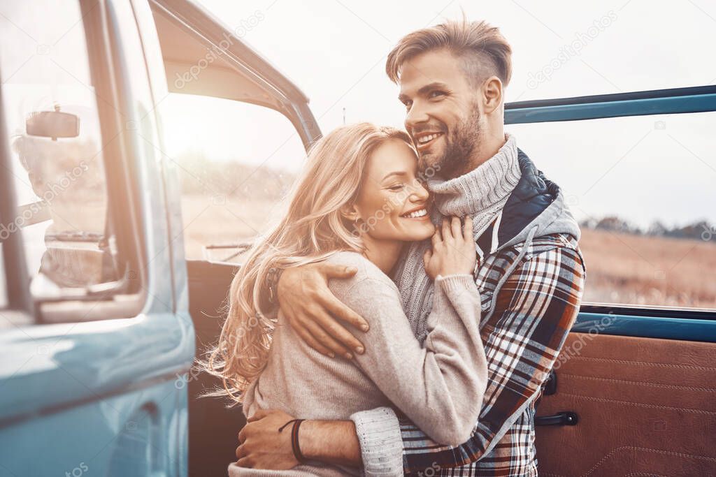 Beautiful young loving couple embracing while standing near minivan outdoors