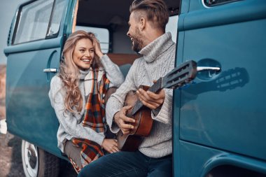 Karavanda vakit geçirirken kız arkadaşına gitar çalan yakışıklı bir genç.