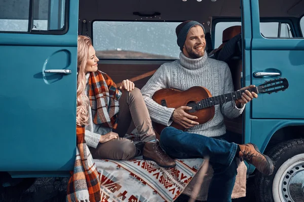 Красивый молодой человек играет на гитаре для своей девушки, проводя время в доме на колесах — стоковое фото