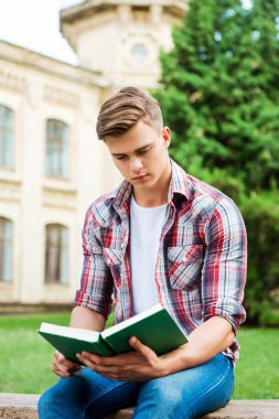 Öğrenci kitap okuma bankta otururken