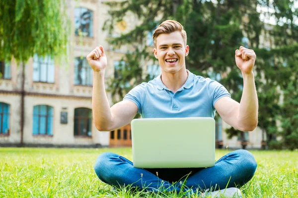 Чоловік піднімає руки сидячи на траві з ноутбуком — стокове фото