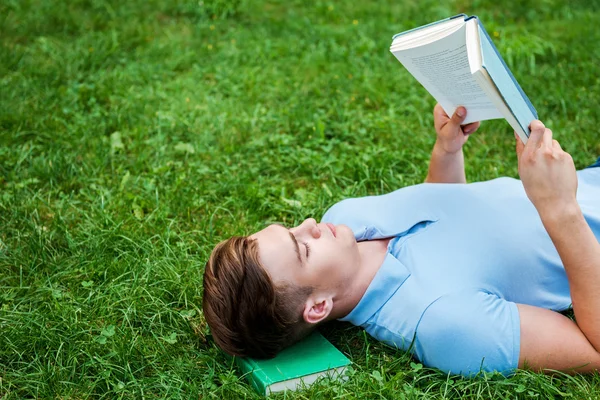 Mann liest Buch, während er im Gras liegt — Stockfoto