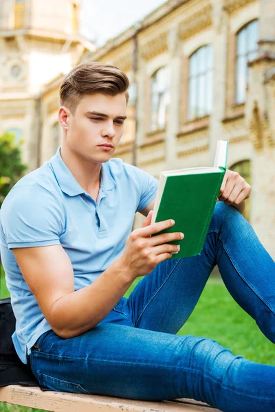 Livro de leitura do estudante enquanto sentado no banco — Fotografia de Stock