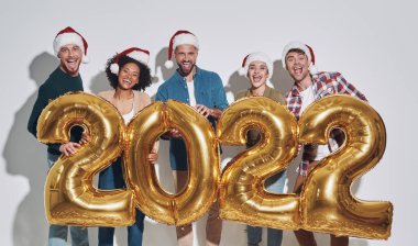 Altın renkli numaralar taşıyan ve gülümseyen Noel şapkalı bir grup güzel insan.