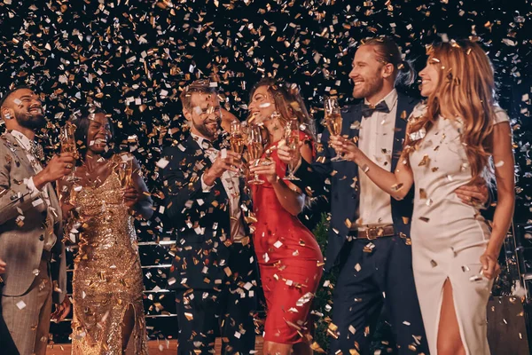 Grupp av vackra människor i formalwear har kul tillsammans med konfetti flyger runt — Stockfoto