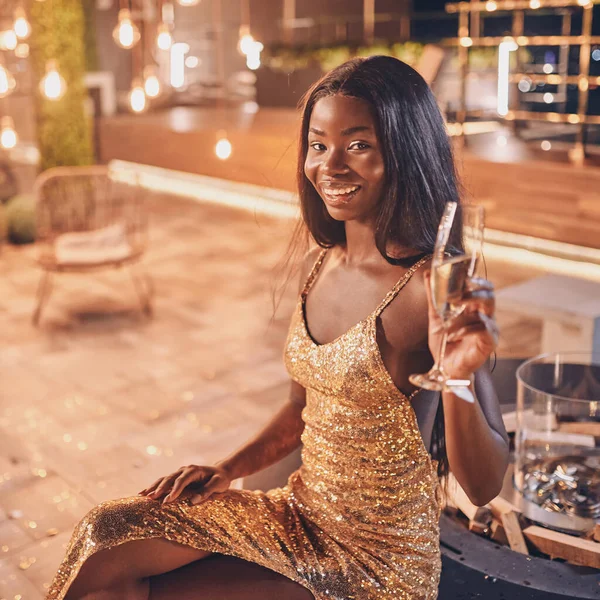 Gyönyörű fiatal afrikai nő estélyi ruhában kezében fuvola pezsgővel és mosollyal — Stock Fotó