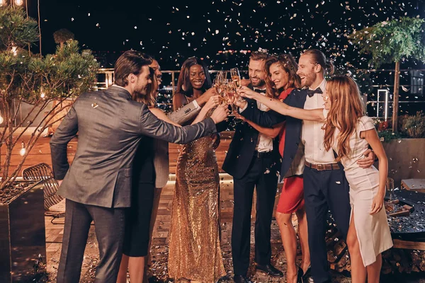 Egy csapat boldog ember ünnepi koccintással pezsgővel, konfettivel mindenfelé. — Stock Fotó