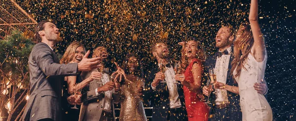 Group of happy people in formalwear having fun together with confetti flying all around — Stock Photo, Image