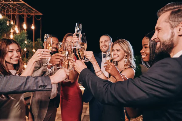 Egy csoport gyönyörű ember ünnepi ruhában pezsgővel és mosollyal, miközben luxusbulin vannak. — Stock Fotó