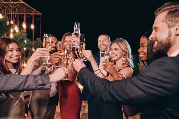 Formalite icabı giyinmiş bir grup güzel insan şampanyayla kadeh kaldırıyor ve lüks bir partide vakit geçirirken gülümsüyor. — Stok fotoğraf